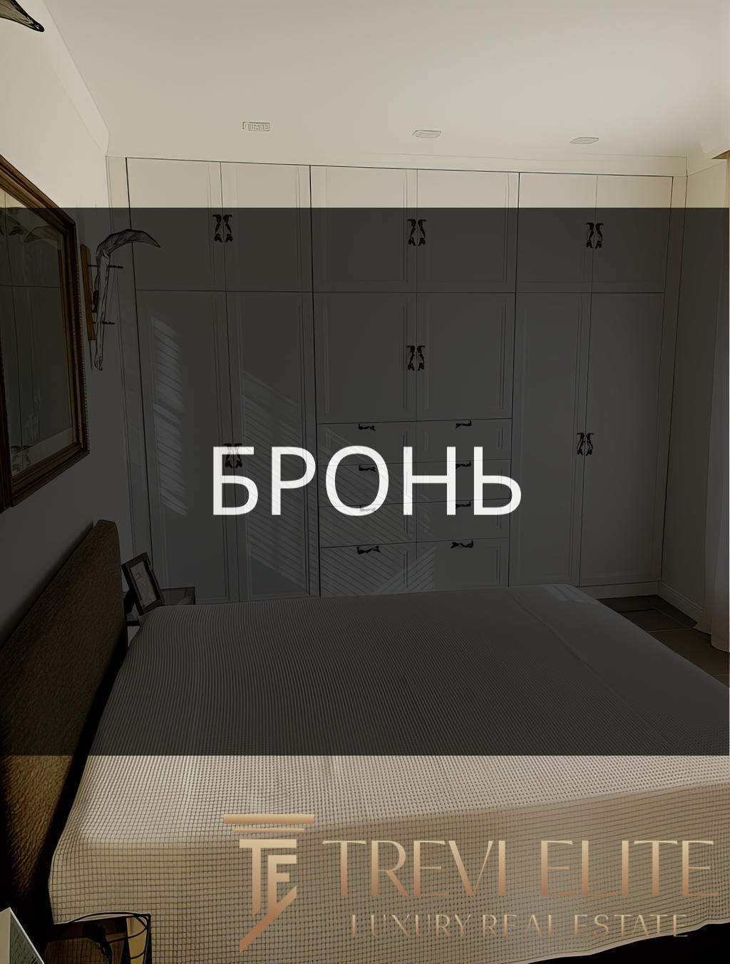 Роскошная спальня с встроенными белыми шкафами, уютной кроватью и стильными декорациями, создающими атмосферу комфорта и современного дизайна в элитной недвижимости.