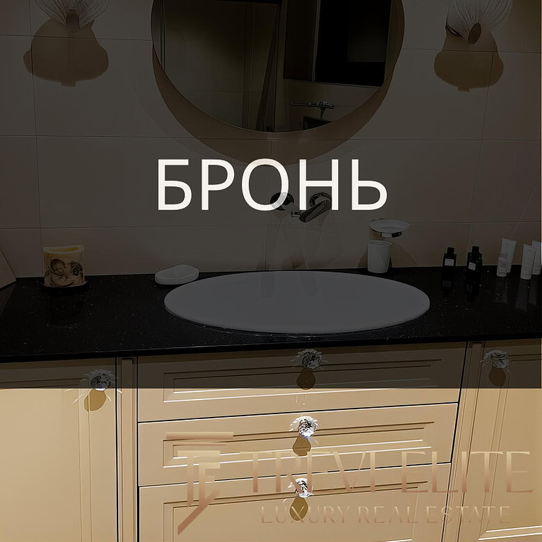 Элегантный интерьер ванной комнаты с зеркальным круглым зеркалом, современным светильником, белым умывальником и эстетичной мебелью, создающей уютную и стильную атмосферу.