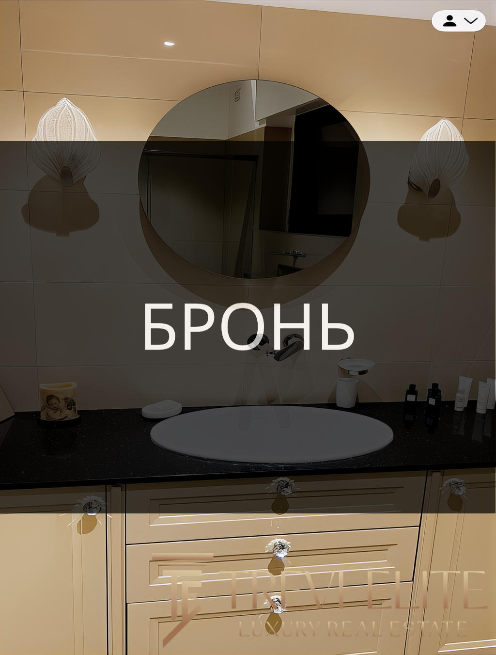 Элегантный интерьер ванной комнаты с зеркальным круглым зеркалом, современным светильником, белым умывальником и эстетичной мебелью, создающей уютную и стильную атмосферу.