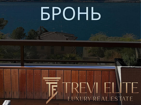 Бронирование пейзажного вида на озеро и горы с балкона с деревянным поручнем и уютным креслом.