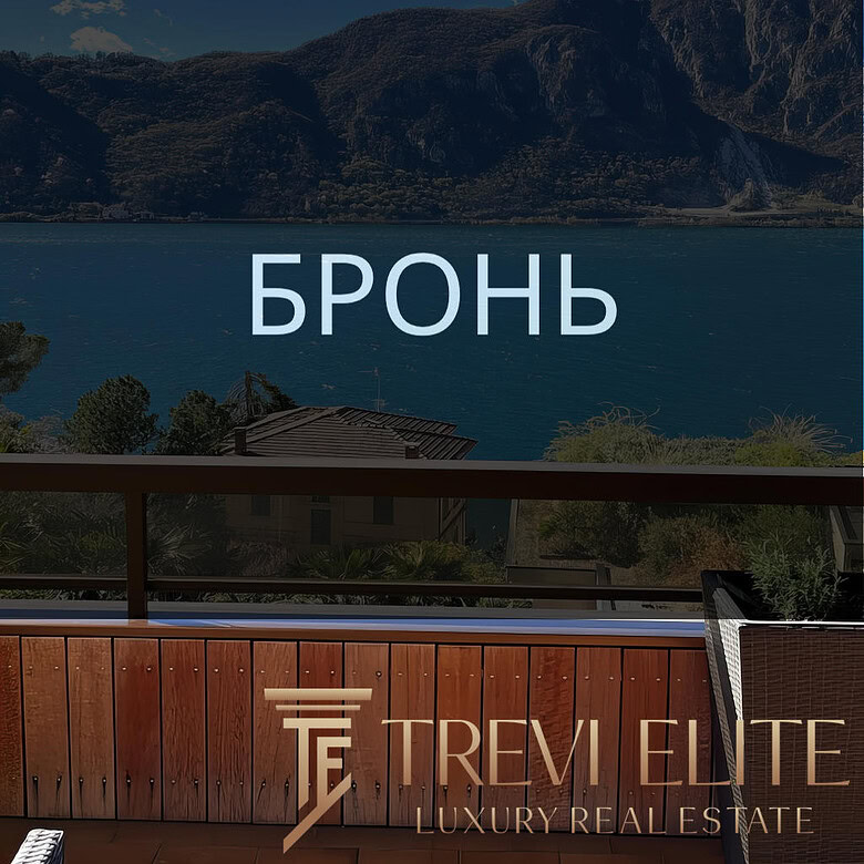 Бронирование пейзажного вида на озеро и горы с балкона с деревянным поручнем и уютным креслом.