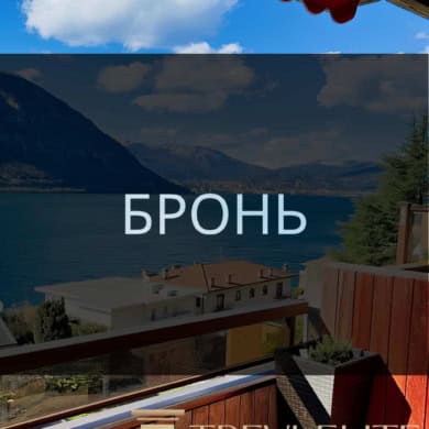 вид на озеро и горы с балкона с деревянным настилом, уютной мебелью и цветущими растениями, панорамный вид на природу и спокойствие, фото демонстрирует роскошные апартаменты у воды, агентство недвижимости Треви Элит.