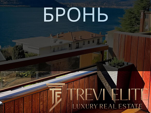 вид на озеро и горы с балкона с деревянным настилом, уютной мебелью и цветущими растениями, панорамный вид на природу и спокойствие, фото демонстрирует роскошные апартаменты у воды, агентство недвижимости Треви Элит.