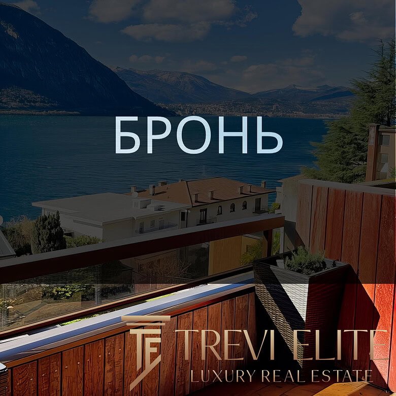 вид на озеро и горы с балкона с деревянным настилом, уютной мебелью и цветущими растениями, панорамный вид на природу и спокойствие, фото демонстрирует роскошные апартаменты у воды, агентство недвижимости Треви Элит.