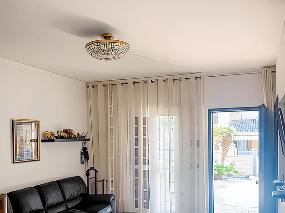 Уютная гостиная с современным интерьером, просторными окнами с белыми шторами и выходом на улицу, компактным диваном черного цвета и стильным освещением.