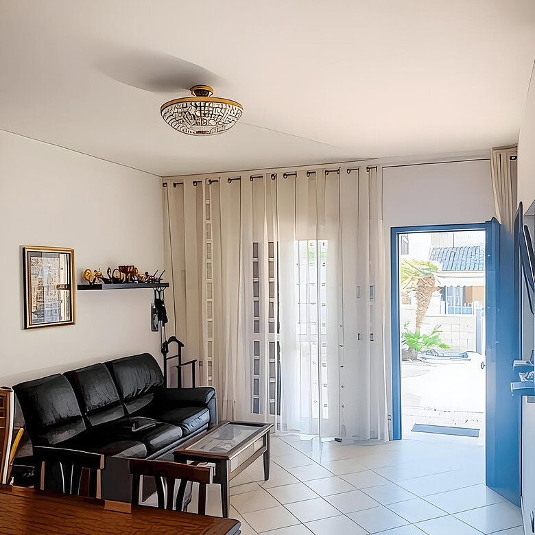 Уютная гостиная с современным интерьером, просторными окнами с белыми шторами и выходом на улицу, компактным диваном черного цвета и стильным освещением.