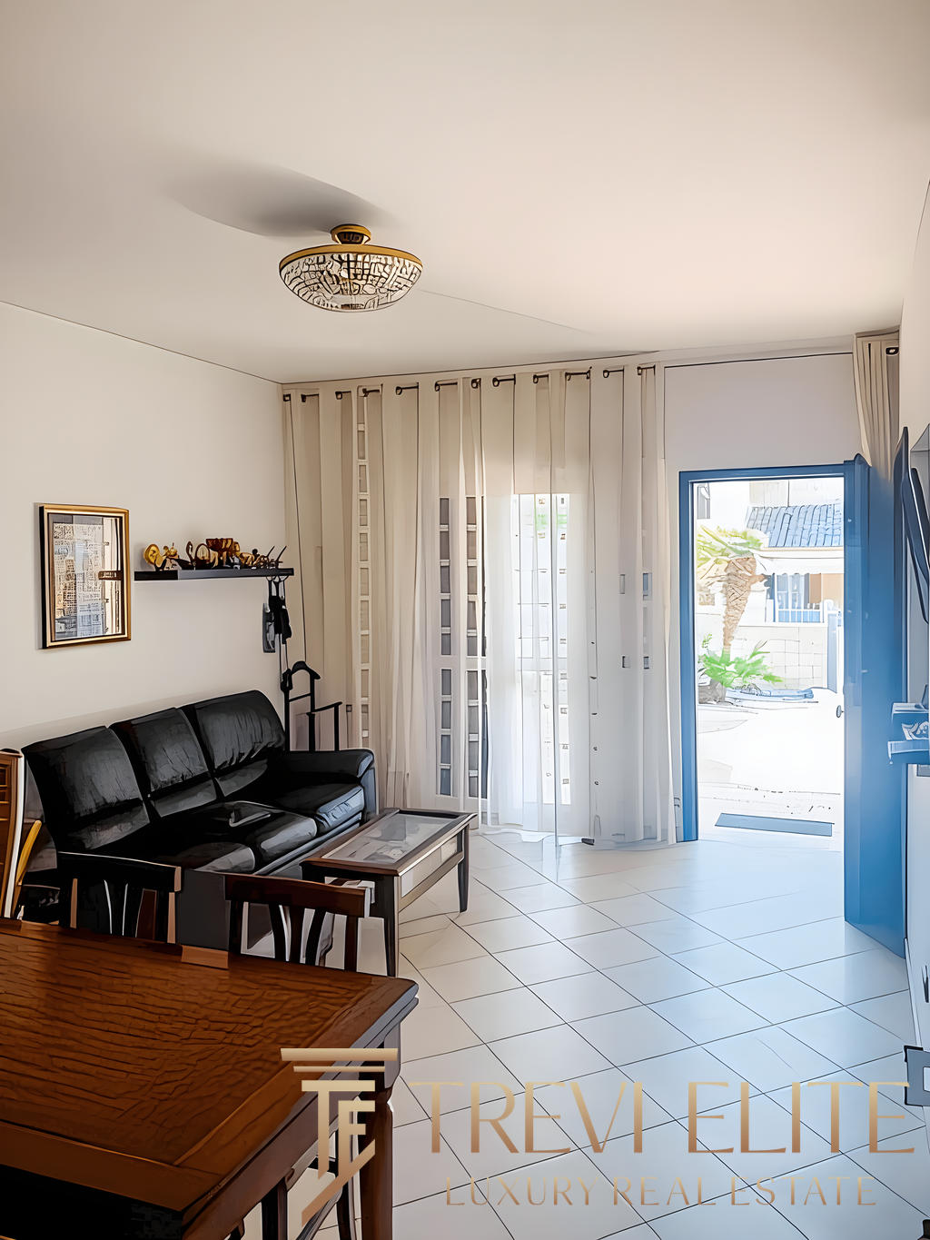 Уютная гостиная с современным интерьером, просторными окнами с белыми шторами и выходом на улицу, компактным диваном черного цвета и стильным освещением.