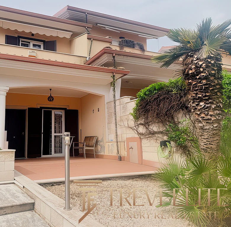 Открытая терраса современного жилого дома с пальмой и зеленью, вход в дом с дверью и зоной отдыха, уличное освещение и уютная атмосфера, стильный дизайн загородного жилья, агентство недвижимости Треви Элит.