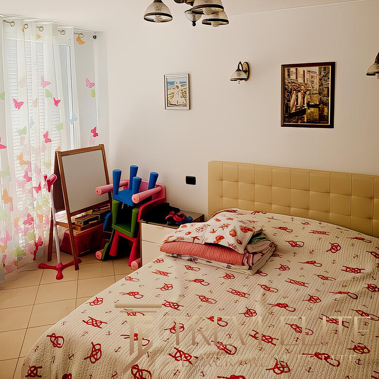 Качественный интерьер светлой спальни с двухспальной кроватью, украшенной постельным бельем с красными узорами, детские игрушки и зеркало у окна, стильная и уютная обстановка.