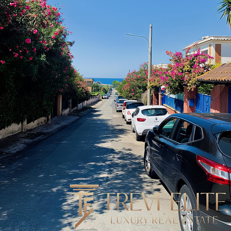 Булыжная улица с парками и цветущими деревьями рядом с морем, перспективы на побережье, автомобили на дороге, солнечный день, спокойная романтичная атмосфера.