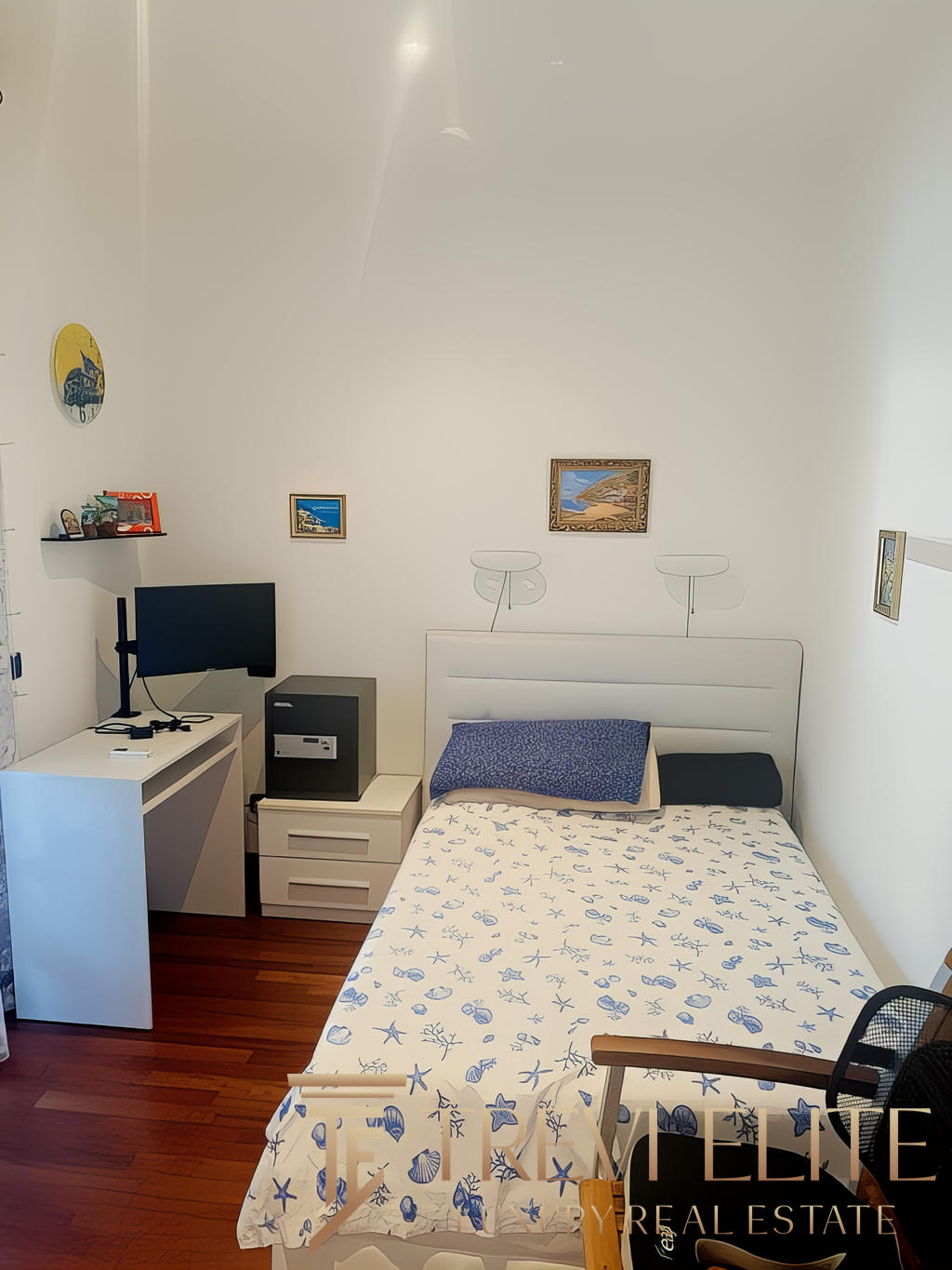 Стильная комната в квартире с белыми стенами, украшенная картинами на морскую тему, с удобной кроватью, письменным столом и современным оборудованием для работы и отдыха.