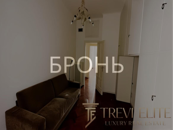 Короткий, уютный коридор с тёмным диваном и встроенными шкафами, светлая стена и дверь, светильник сверху, в минималистском стиле, интерьер современный, комфортный, пространство организовано эргономично, подходит для комфортного проживания.