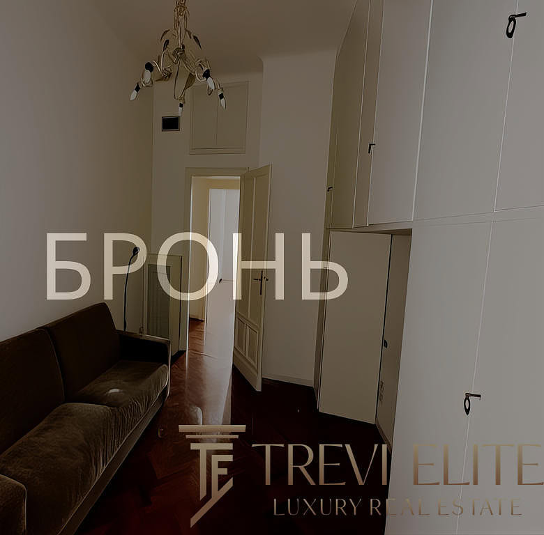 Короткий, уютный коридор с тёмным диваном и встроенными шкафами, светлая стена и дверь, светильник сверху, в минималистском стиле, интерьер современный, комфортный, пространство организовано эргономично, подходит для комфортного проживания.