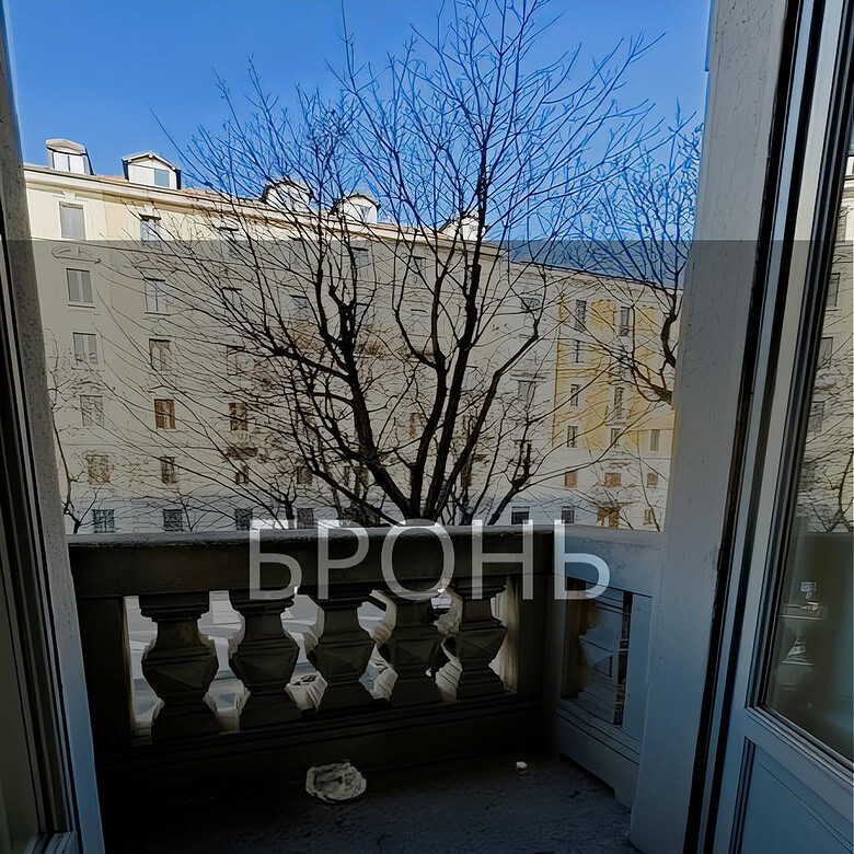 Вид из окна на зимний двор с деревьями и многоэтажными зданиями, солнечный день, красивый городской пейзаж, балкон с классической балюстрадой, просторное помещение, светлый интерьер.