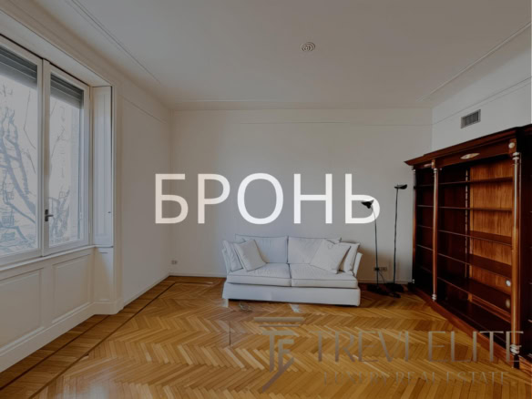 Современная уютная гостиная с деревянным полом и большой книгой полкой, светлым диваном, окнами и минималистичным дизайном.