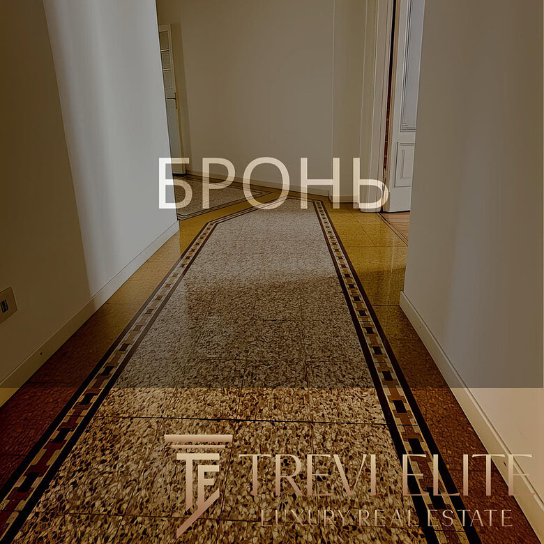 Высококачественный интерьер коридора в современном жилом доме. Теплое освещение, гладкие стены и укороченный ковровый дорожка создают уютную атмосферу. Идеальное изображение для риелторского агентства Треви Элит.