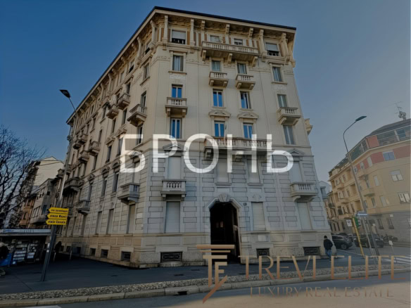 Высокий дом в стиле классической архитектуры с балконами и декоративными элементами на фасаде, расположенный на городской улице с уличными фонарями и прохожими.