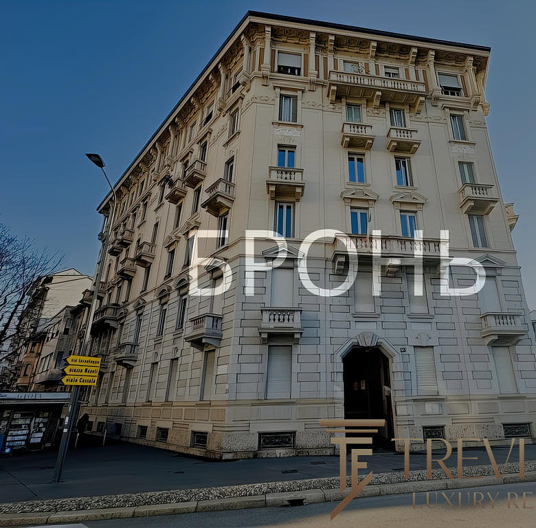 Высокий дом в стиле классической архитектуры с балконами и декоративными элементами на фасаде, расположенный на городской улице с уличными фонарями и прохожими.