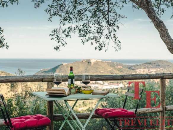 Уютный стол с вином и закусками на террасе с видом на море и холмы, идеально для романтического ужина или отдыха с природой.