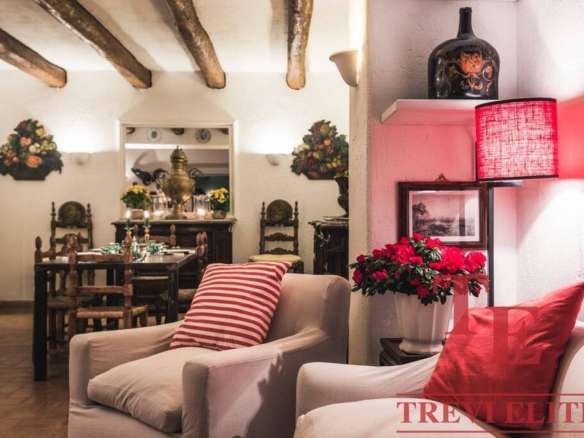 Уютная гостиная с антикварной мебелью, мягким креслом, ярким освещением и цветами в вазе, создающая тепло и комфорт в роскошной итальянской недвижимости.