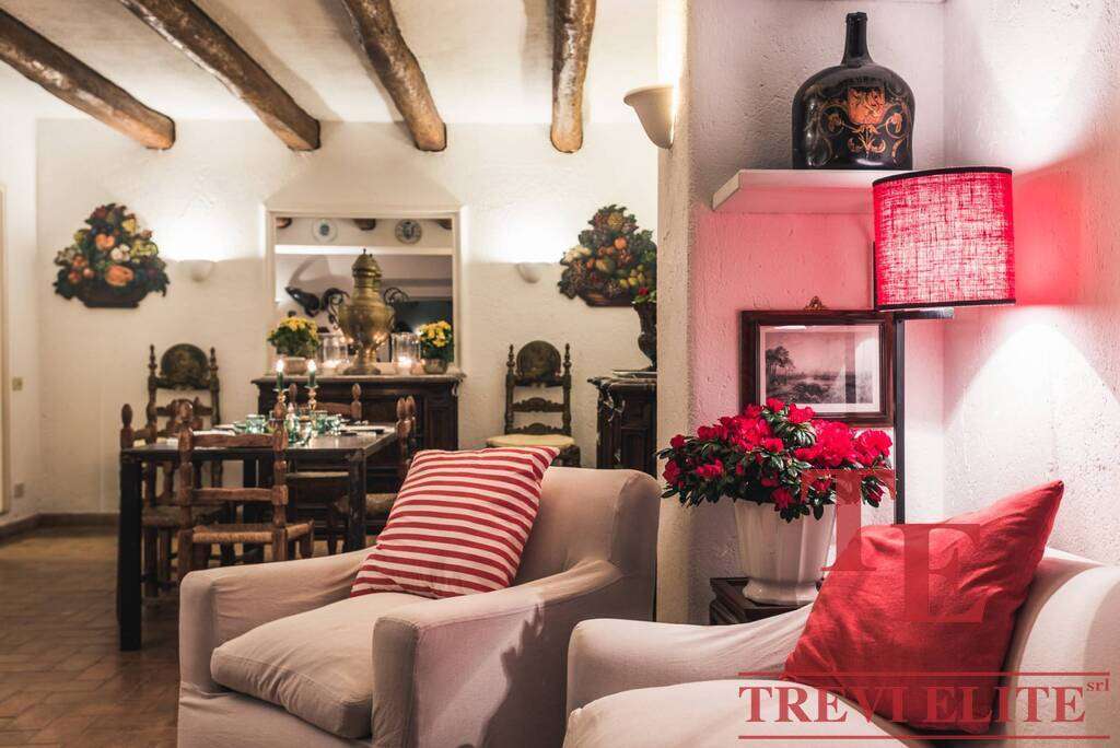 Уютная гостиная с антикварной мебелью, мягким креслом, ярким освещением и цветами в вазе, создающая тепло и комфорт в роскошной итальянской недвижимости.