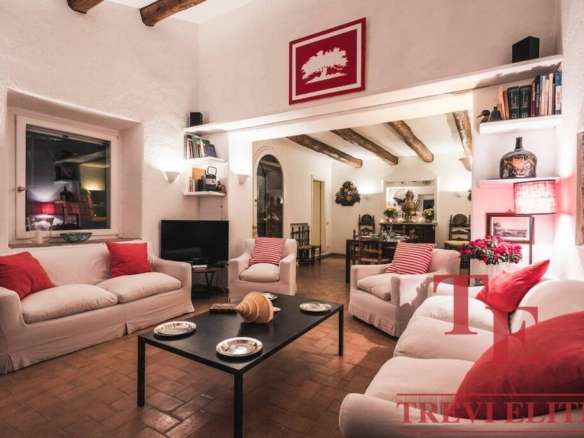 Элегантная гостиная с белыми диванами и красными подушками, уютным освещением, декором и камином, идеально подходит для комфортного отдыха в роскошной недвижимости.