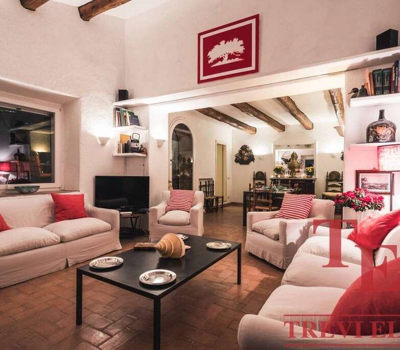 Элегантная гостиная с белыми диванами и красными подушками, уютным освещением, декором и камином, идеально подходит для комфортного отдыха в роскошной недвижимости.