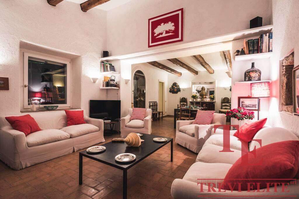 Элегантная гостиная с белыми диванами и красными подушками, уютным освещением, декором и камином, идеально подходит для комфортного отдыха в роскошной недвижимости.