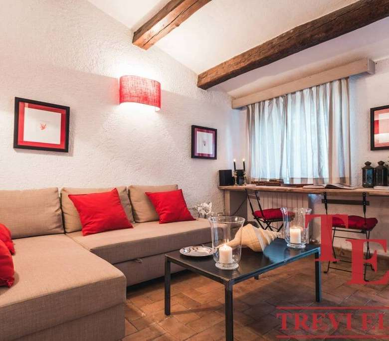 Теплая уютная гостиная с мягким диваном и красными подушками, стильной мебелью и декоративным освещением, идеально подходящая для элитной недвижимости и комфортного отдыха.