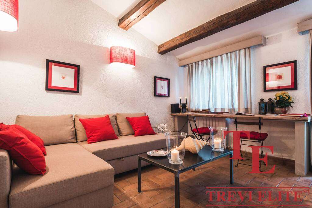 Теплая уютная гостиная с мягким диваном и красными подушками, стильной мебелью и декоративным освещением, идеально подходящая для элитной недвижимости и комфортного отдыха.