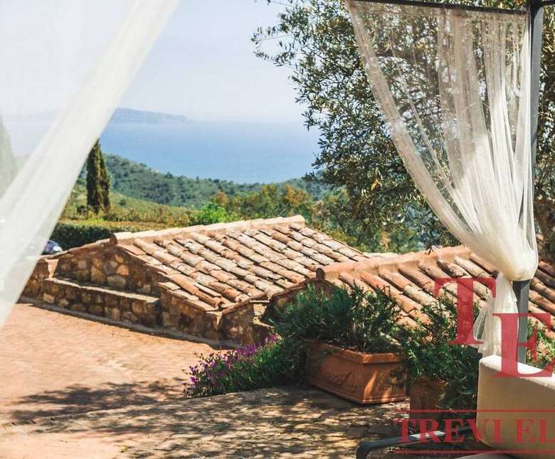 Роскошный вид на зеленые холмы и море с террасы итальянской виллы, украшенной шторками и цветами, создающий атмосферу спокойствия и уединения.
