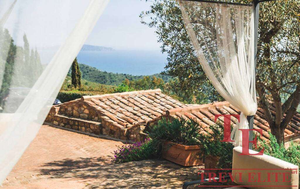 Роскошный вид на зеленые холмы и море с террасы итальянской виллы, украшенной шторками и цветами, создающий атмосферу спокойствия и уединения.