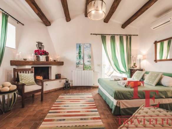 Уютная спальня с деревянными потолочными балками, зелеными занавесками и мягкой мебелью, создающая атмосферу комфорта и роскоши в элитной недвижимости.