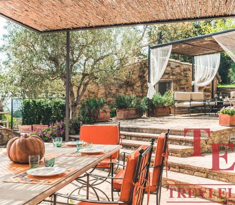 Уютный уличный обеденный уголок на террасе, окруженный зеленью и зелеными деревьями. Эргономичная мебель и декоративные элементы создают атмосферу комфорта и уединения под деревянным навесом.