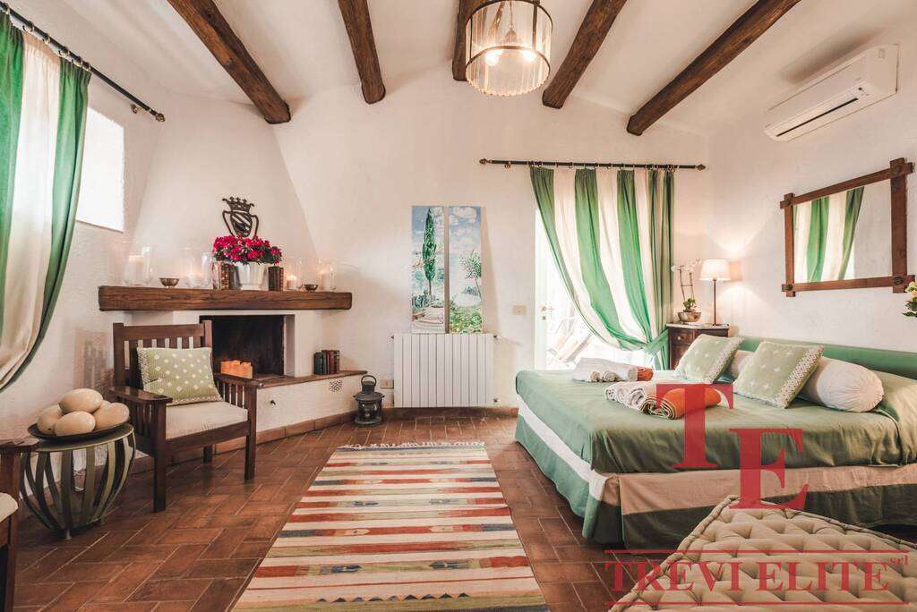 Уютная спальня с деревянными потолочными балками, зелеными занавесками и мягкой мебелью, создающая атмосферу комфорта и роскоши в элитной недвижимости.