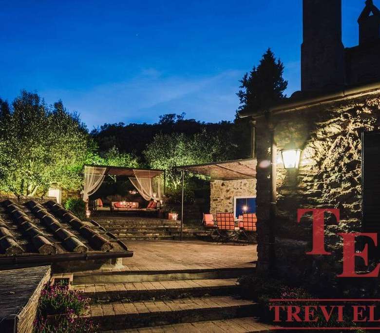 Уединённый уютный дворик у роскошной загородной недвижимости с мягким освещением и зоной отдыха на свежем воздухе. Отличное место для вечерних мероприятий и расслабления в окружении природы.