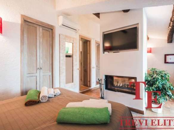 Уютная спальня с камином, современными телевизором и кондиционером, теплым освещением и аккуратной мебелью, созданной для комфортного отдыха и стильного интерьера в элитной недвижимости.