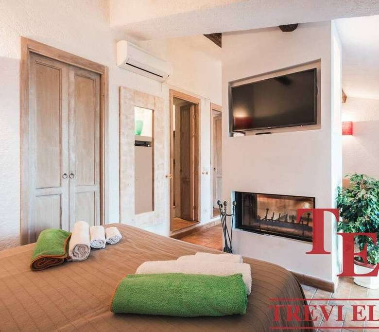 Уютная спальня с камином, современными телевизором и кондиционером, теплым освещением и аккуратной мебелью, созданной для комфортного отдыха и стильного интерьера в элитной недвижимости.