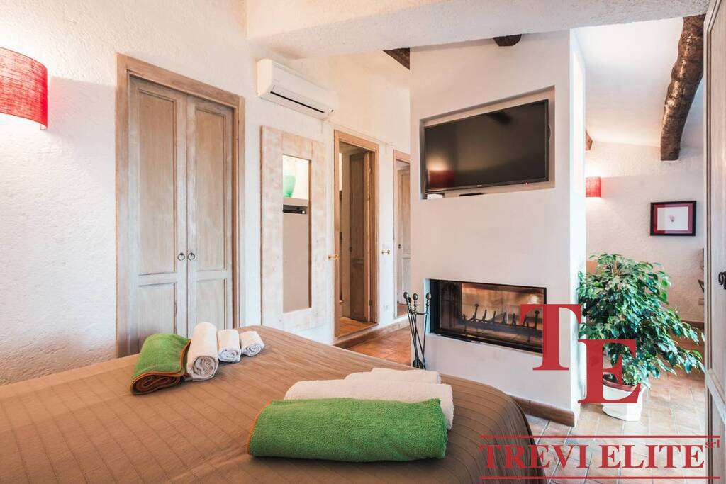 Уютная спальня с камином, современными телевизором и кондиционером, теплым освещением и аккуратной мебелью, созданной для комфортного отдыха и стильного интерьера в элитной недвижимости.