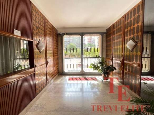 Элегантный интерьер входной зоны с деревянными панелями, большими окнами и комнатными растениями, создающими уютную атмосферу в роскошной недвижимости.