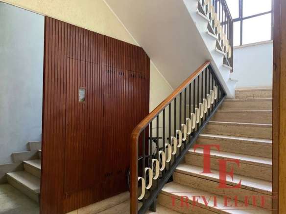 Элегантная лестница в жилом доме с современным деревянным перилами и коваными элементами, ярко освещена естественным светом из окна, создавая уютную атмосферу.