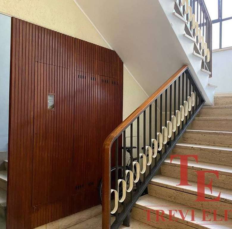 Элегантная лестница в жилом доме с современным деревянным перилами и коваными элементами, ярко освещена естественным светом из окна, создавая уютную атмосферу.