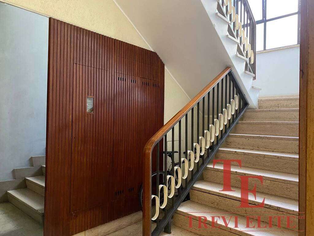 Элегантная лестница в жилом доме с современным деревянным перилами и коваными элементами, ярко освещена естественным светом из окна, создавая уютную атмосферу.