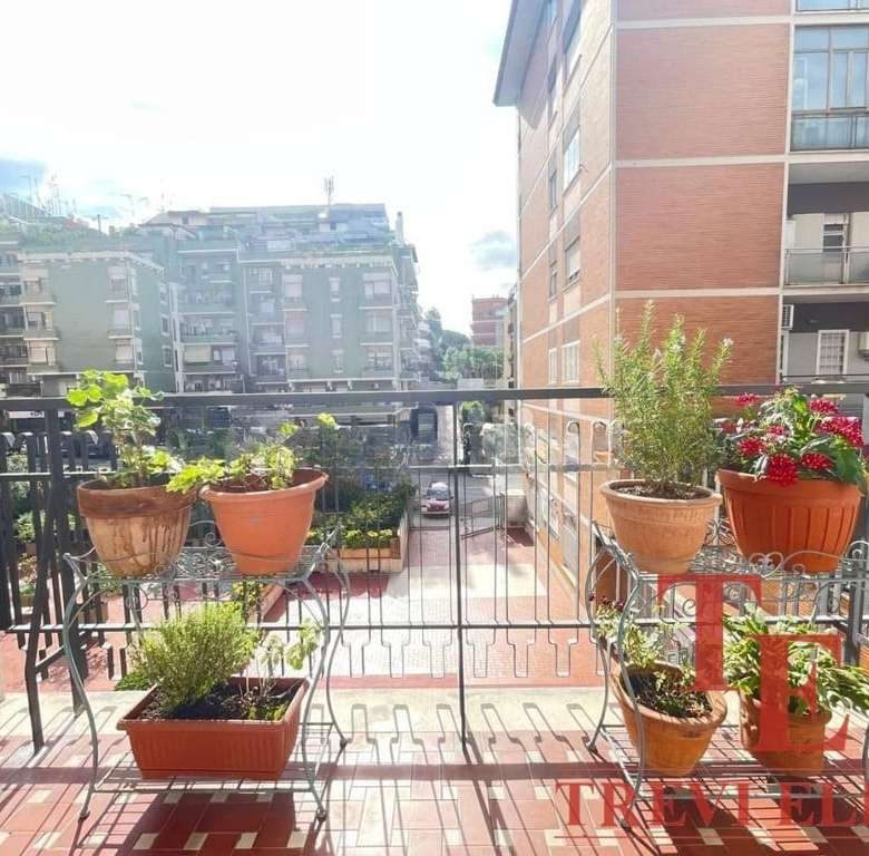 Ящик с цветами на балконе жилого комплекса, вид на городские здания и улицы.