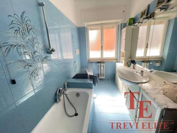 Уютная ванная комната с голубыми плитками, большой зеркальной рамой и естественным светом от окна, идеально подходит для роскошного жилья.