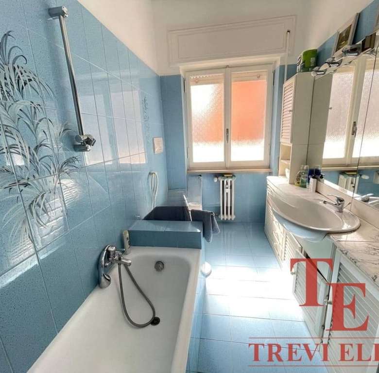 Уютная ванная комната с голубыми плитками, большой зеркальной рамой и естественным светом от окна, идеально подходит для роскошного жилья.