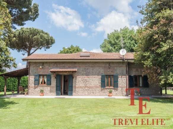 Испанский загородный дом с каменной облицовкой, окруженный зелёным газоном и высокими деревьями, под ясным небом, сочетающий элегантность и уединение, эксклюзивное предложение от Треви Элит.