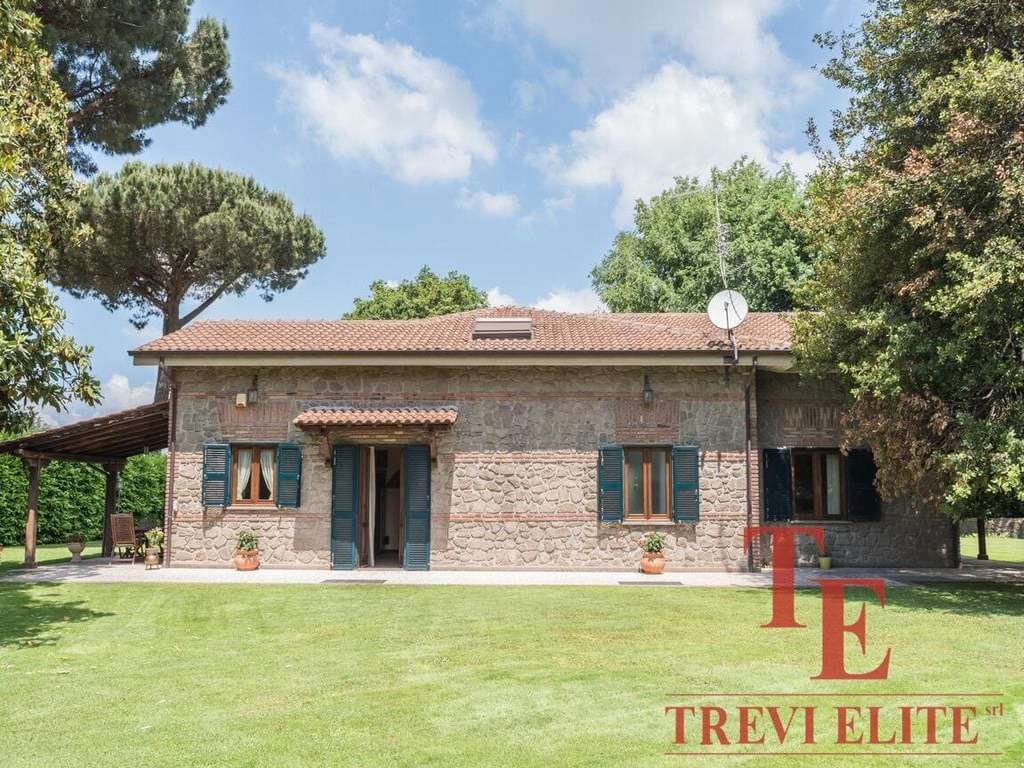 Испанский загородный дом с каменной облицовкой, окруженный зелёным газоном и высокими деревьями, под ясным небом, сочетающий элегантность и уединение, эксклюзивное предложение от Треви Элит.