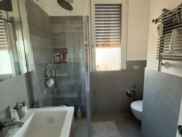 Современная ванная комната с душевой кабиной, раковиной и окном с ролл-шторами, выполненная в стильных нейтральных оттенках, идеально подходит для роскошной жизни.