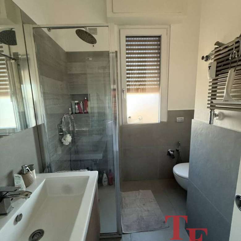 Современная ванная комната с душевой кабиной, раковиной и окном с ролл-шторами, выполненная в стильных нейтральных оттенках, идеально подходит для роскошной жизни.